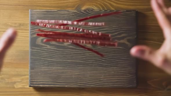 Man Hands Drop Jerked Red Fish Sticks Onto Wooden Board