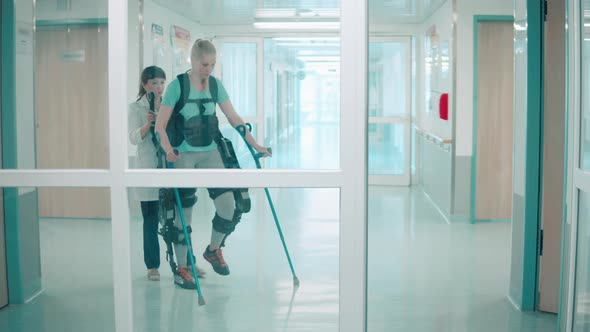 Young Woman is Walking in the Exosuit with Doctor's Help