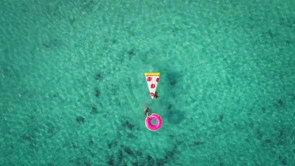 Aerial zoom view of two young girls swimming and playing in sea with inflatables.