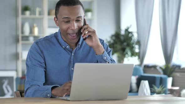 Young African Man Talking on Phone at Workplace