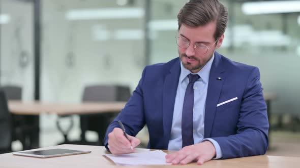 Serious Young Businessman Writing on Paper 