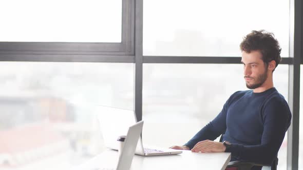 Young Intelligent Caucasian Businessman Sitting at Office Table in Evening