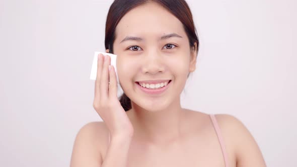 Happy Asian girl using cotton pad applying facial wipe on her face, removing makeup.