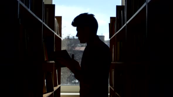 Silhouette of Young Student Reading a Book in a Library