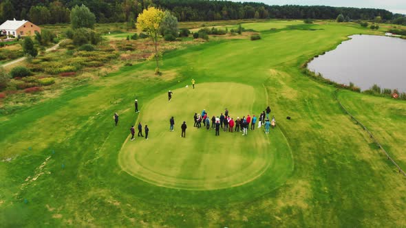 A Bunch of Young and Middleaged Adults Standing on a Juicy Field Playing Golf on a Cloudy Day in a