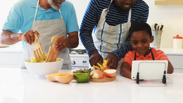 Boy showing digital tablet to his father and grandfather while preparing salad