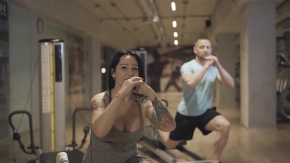 Attractive Female Personal Trainer Showing Exercise To Blurred Man Repeating at the Background