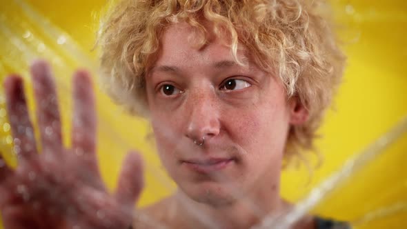 Closeup Face of Young Androgynous Man Looking at Camera Touching Wet Food Film Posing at Yellow