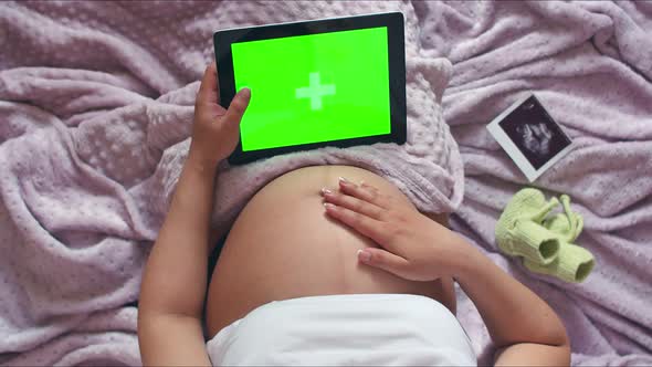 A Pregnant Woman Strokes Her Stomach and Holds a Digital Tablet with a Chromakey, A Pregnant Girl