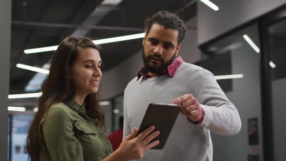 Diverse female and male work colleagues standing looking at tablet together and talking