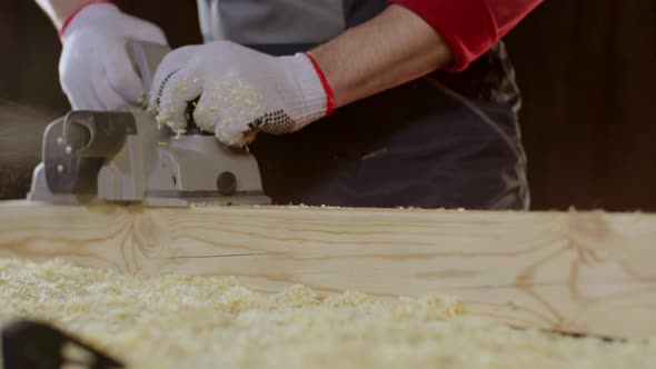 Close-up Hands of Joiner Using Electric Planer with Wooden Blank in Workshop.