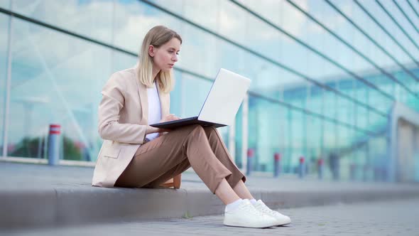 young business woman sitting on the sidewalk and working on laptop