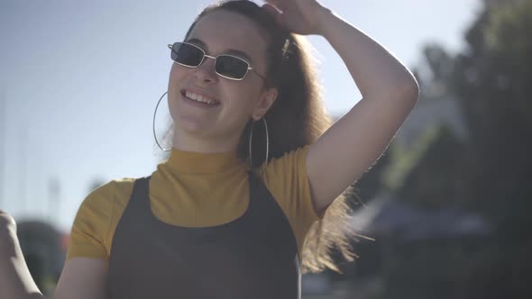 Close-up of Charming Coquette Caucasian Young Woman in Sunglasses Posing in Sunlight Outdoors