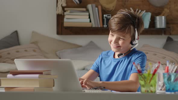 smiling student boy studying at home with remote school connected to computer on the web