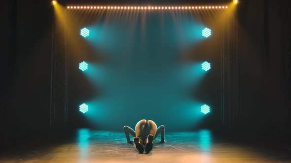 Silhouette of Slim Athletic Woman Shaking Her Ass While Sitting on Floor in Dark Studio with Blue