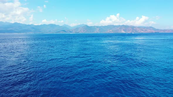 Blue wavy sea around mountain island brighten by morning sunlight in Lombok, Indonesia, aerial panor