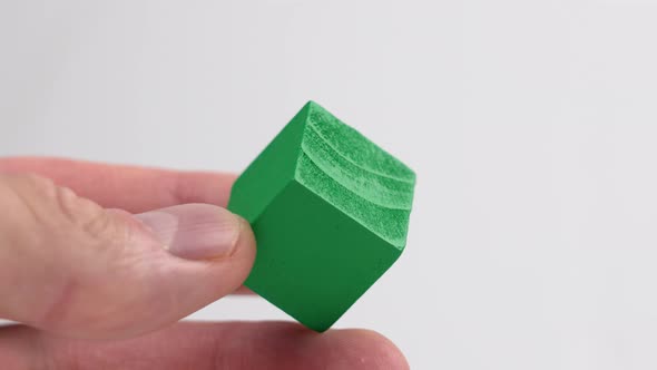 A hand holding a green wooden toy cube on a white background