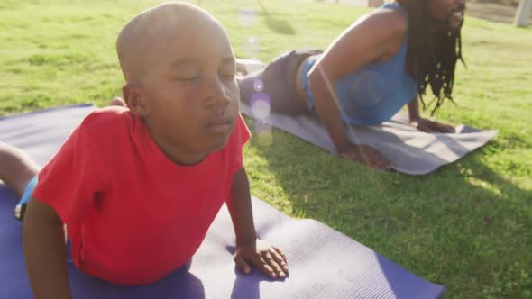 Video of african american son and father practicing yoga on grass on sunny day