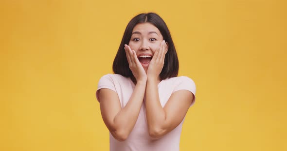 Young Surprised Woman Touching Cheeks, Opening Mouth in Amazement, Orange Studio Background