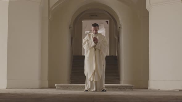 Priest in White Robe Praying to God at Church Entrance