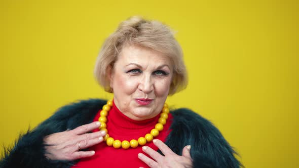 Closeup Portrait of Confident Caucasian Senior Woman in Fur Coat Dancing on Yellow Background