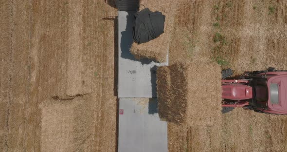 Red tractor loading Hay bales onto a parked truck, Aerial footage.