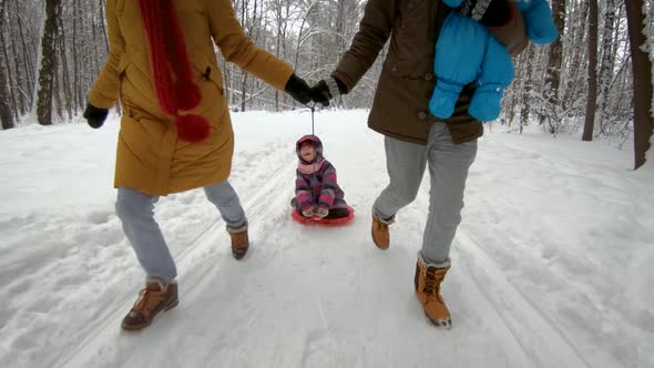 Young parents running with their children on sled in winter park