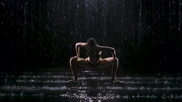 Woman Doing Yoga Exercises in the Pouring Rain in a Dark Studio. Spotlight Illuminates the Surface