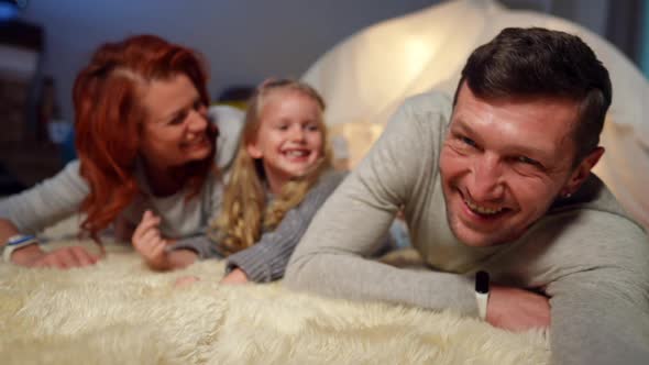 Portrait of Happy Man Laughing Taking Selfie with Daughter and Wife Lying at Tent in Living Room