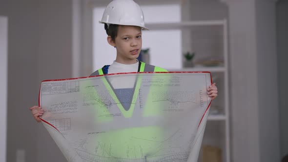 Medium Shot Portrait of Confident Boy in Hard Hat Talking Standing with Architectural Blueprint