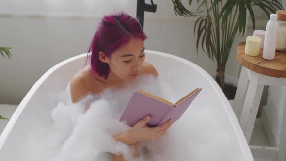 Young Asian Woman Reading Book in Bathtub