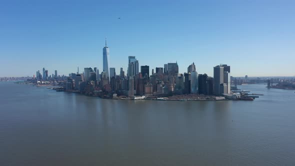 An aerial view of New York Harbor on a sunny day with blue skies. The drone camera facing lower Manh