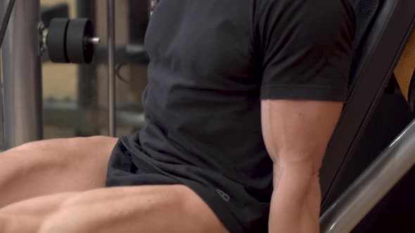 Closeup View of the Man Athlete with Muscular Legs Working Out at the Gym Leg Curl Trainer