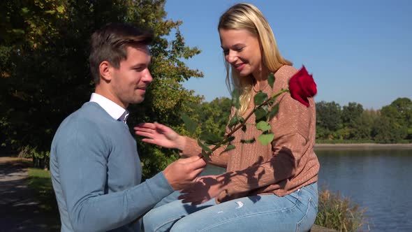 A Man Gives a Red Rose To His Girlfriend in a Park on a Sunny Day