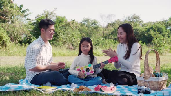 Happy family picnic. little girl playing ukulele with her parents (Father, Mother) during picnic