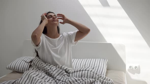 Pretty Young Woman Is Sitting in Sunny Bedroom in Morning, Stretching Hands Up