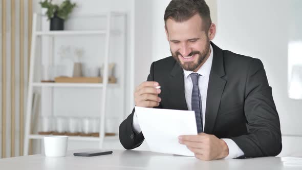 Businessman Celebrating Success While Reading Documents in Office