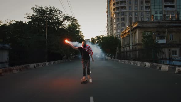 Young Man in Bandana on Face and Flag of USA Tied on Neck is Skateboarding Along Deserted Street