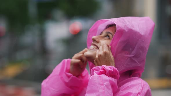 Young Smiling Woman with a Pink Raincoat While Enjoying a Walk Through the City on a Rainy Day