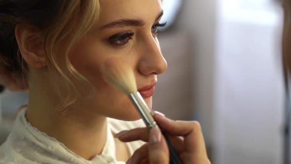 Closeup of Makeup Artist Putting Rouge on Cheek of Pretty Woman Using Brush