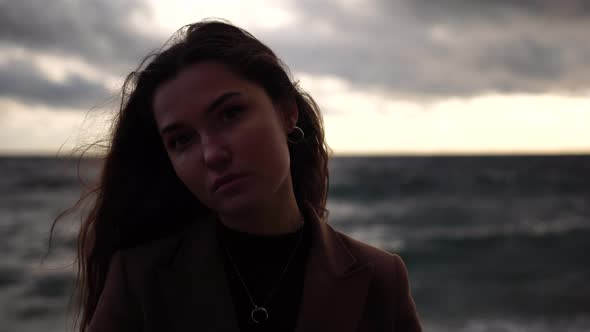 Young Beautiful Sensual Woman in a Brown Long Coat Posing at the Beach on Sunset Time