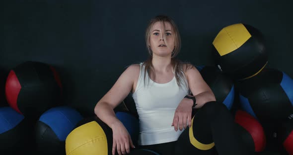 Portrait of Beautiful Young Caucasian Athlete Woman Sitting on Gym Floor Among Balls Exhausted After