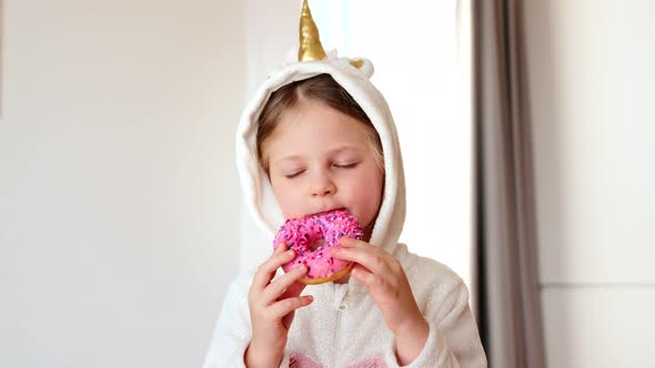 Little kid preschool girl in a unicorn costume eating sweet pink donut