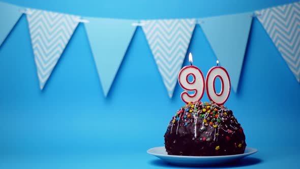 chocolate birthday cake with a burning candle number ninety, 90 on a blue background. Copy space. pl