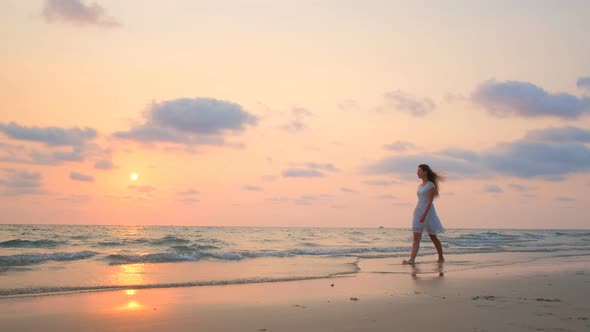 Young Beautiful Girl in a White Dress Walking Along the Beach