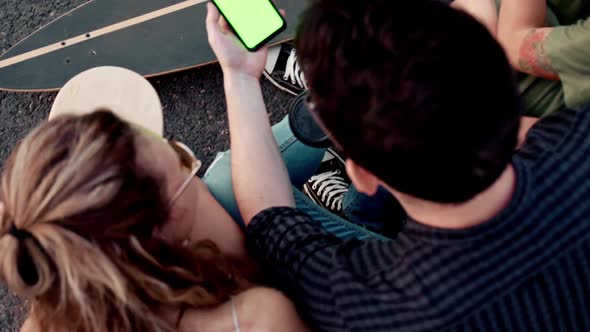 Young Millennial Friends Sitting Outside with Coffee and Looking at Green Screen Phone in Park