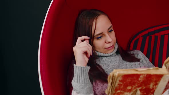 Young Woman Reads Old Book Sitting in Ball Chair