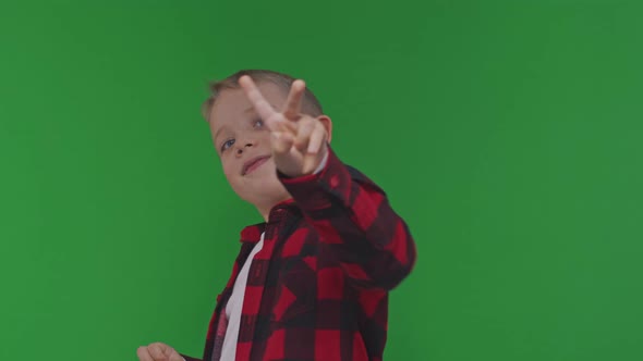 The Cute Kid Boy Rejoices and Showes Victory Sign on Isolated Green Background