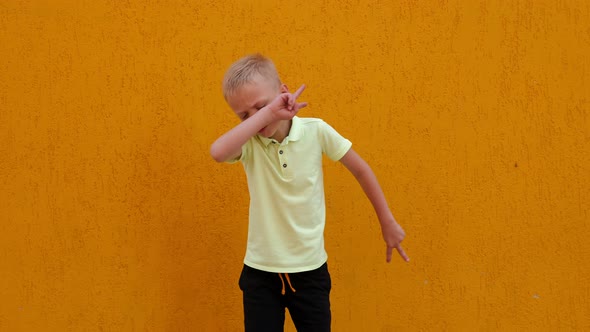 A Little Cheerful Boy Jumps and Has Fun Against the Background of a Yellow Wall