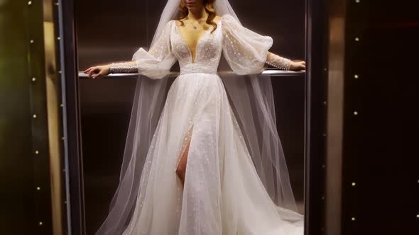 A Beautiful Bride in a White Wedding Dress Stands in the Elevator